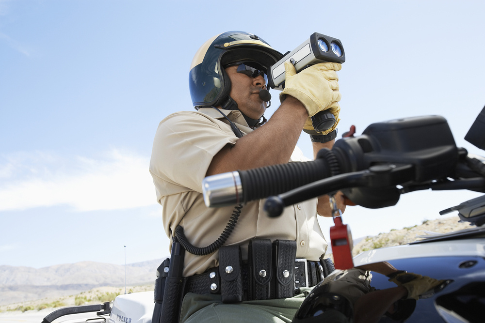 A police officer in a speeding enforcement zone uses a radar gun to detect speeders.