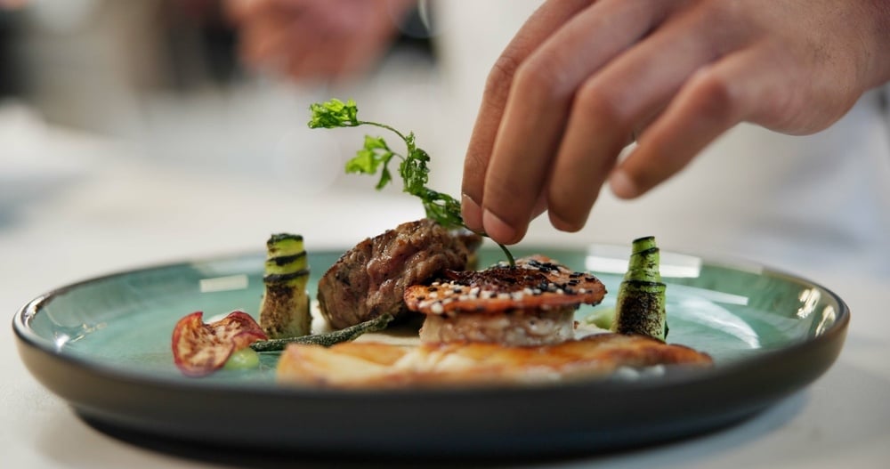 A chef adds garnish to a plate to maximize its value.