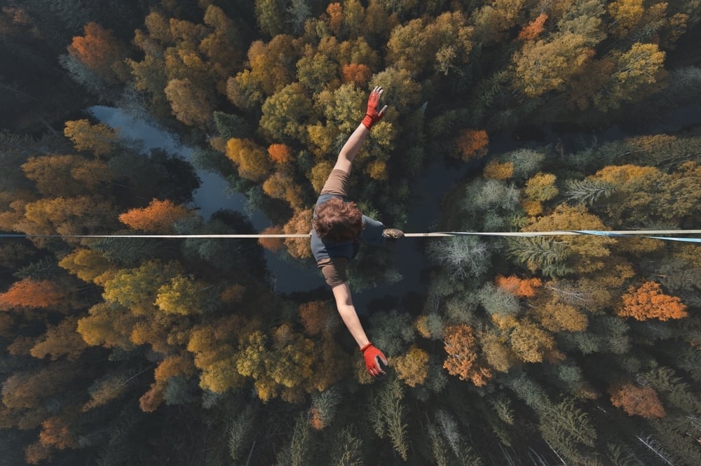 A person walks a tightrope high above a forest; just as CMS must walk a tightrope in stabilizing the ACA Marketplaces.